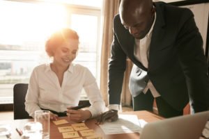 Young business colleagues in conference room discussing manpower resources. Businesswoman sitting with names on adhesive notes and businessman standing by.